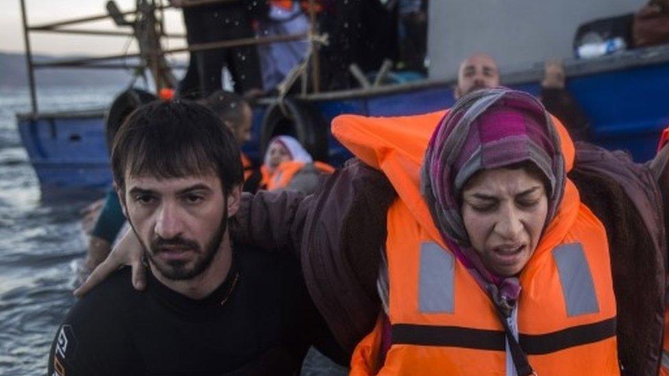 A volunteer helps one of about 50 migrants to disembark from a vessel after their arrival from the Turkish coast to the north-eastern Greek island of Lesbos (01 December 2015)