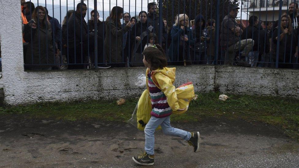 A refugee girl runs as local residents hold a protest outside a school at the Greek village of Profitis some 35 kilometers (22 miles) east of Thessaloniki, on Monday, Oct. 10, 2016.