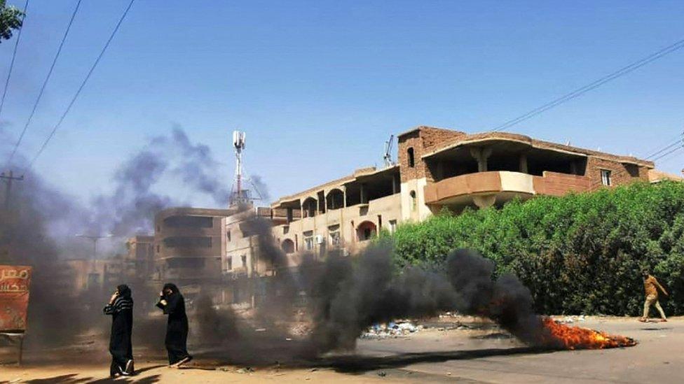 Sudanese women walk in front of tyres set ablaze by anti-coup demonstrators in the capital Khartoum, following calls for civil disobedience to protest last month's military coup, on November 7, 2021.