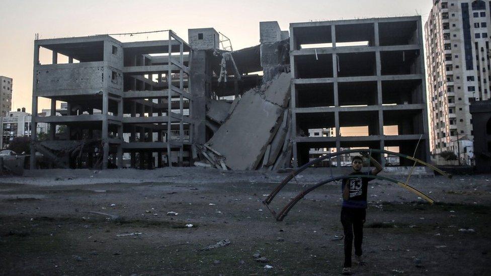 A Palestinian carries a destroyed swing at the park near a building after Israeli air strikes, at central Gaza City, 14 July 2018