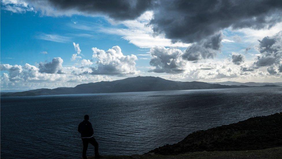 A man looks at the Greek island of Lesbos from the Turkish coastline, during a cloudy and windy day on March 4, 2016