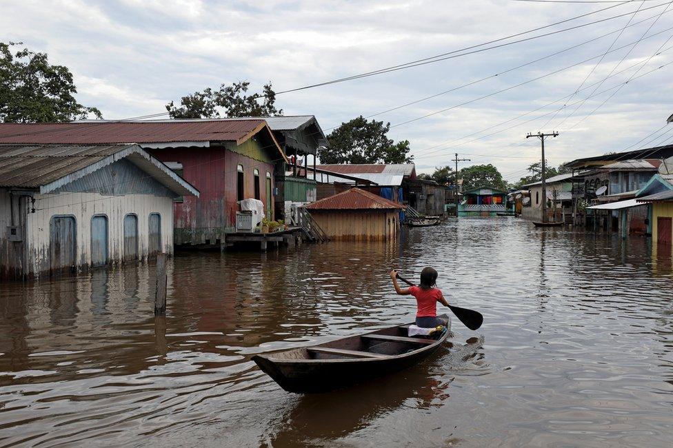 A girl paddles her canoe through a street flooded by the rising Solimoes river