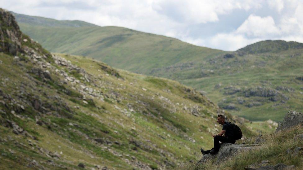 A man sits on a rock and looks on in the Pen y Pass at the foot of Snowdon