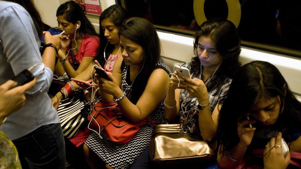 Indian women use their smartphones as they travel in the metro carriage reserved for women in New Delhi on July 14, 2015