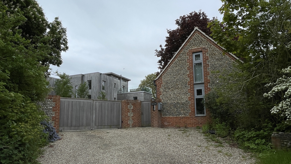 Arcady house, showing wooden structured house behind closed wooden gate and gravel driveway