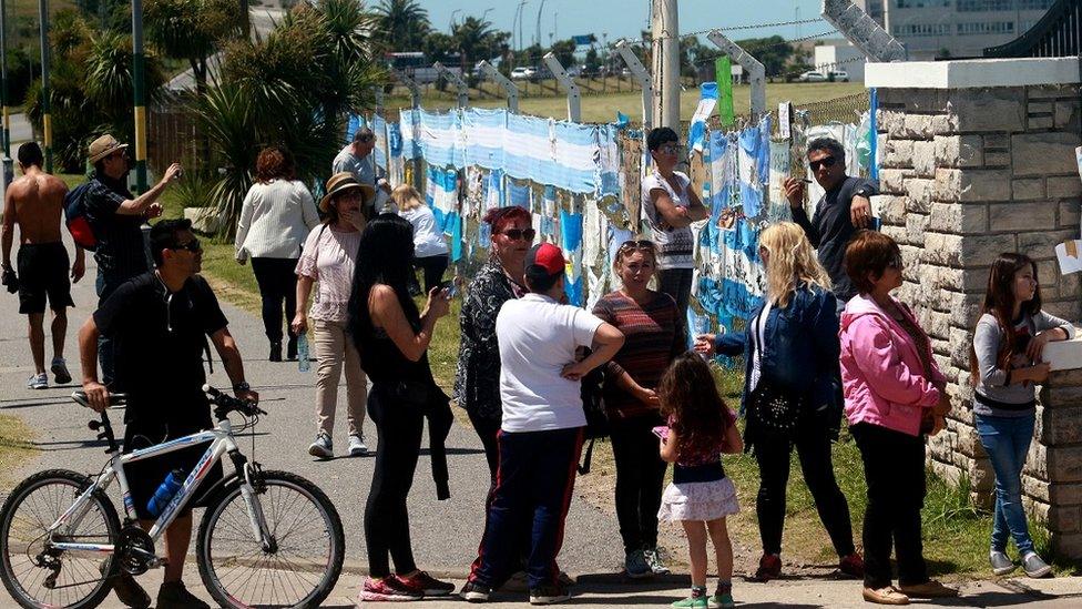 people gathering around the signs on a fence at the naval base