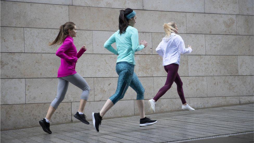 Rear view of three woman jogging on footpath along side a wall. - stock photo