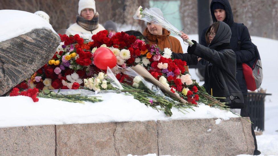 People laying floral tributes at a stone covered in snow