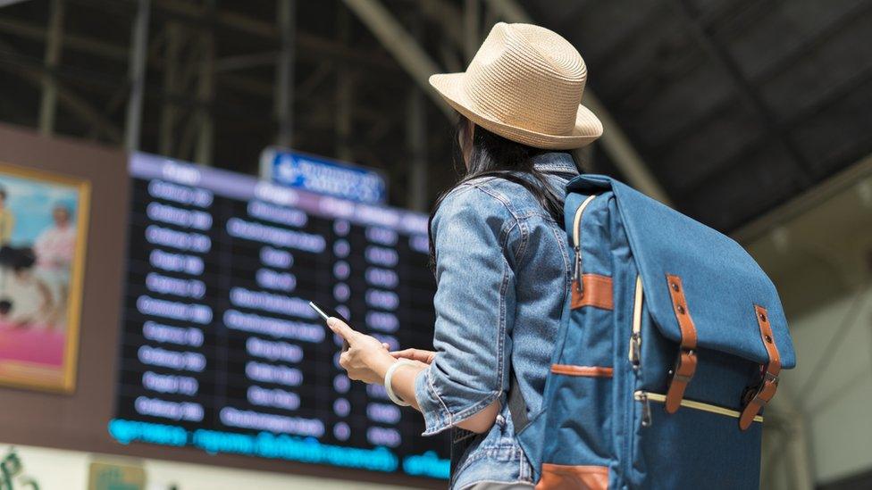 A woman pictured from behind in an airport looking up at a departures board