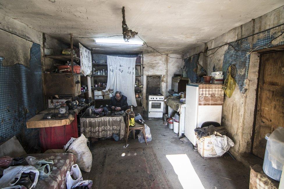 A shoemaker sits in his workshop adjacent to his home