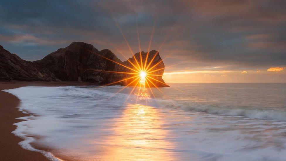 The sun rises through the arch at Durdle Door