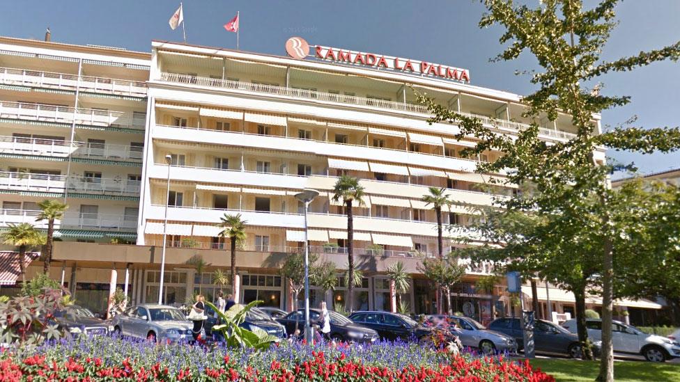 A Google maps street view image shows a multi-story hotel with flowers and trees out front