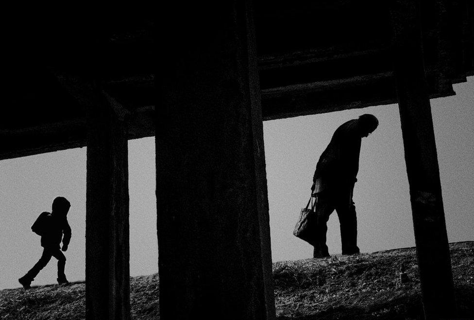 A young boy and old man walk up a slope by Marko Visacki