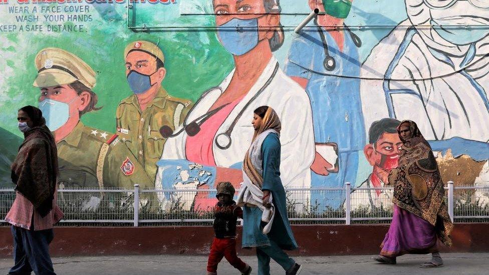 Women walk past a graffiti amidst the spread of the coronavirus disease (COVID-19) in New Delhi, India, February 7, 2022