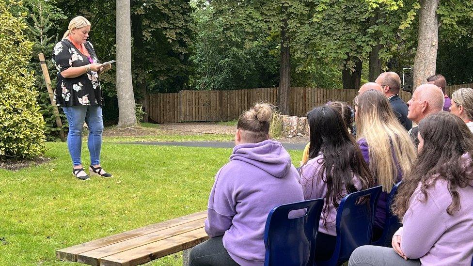 Holly's mum speaks in front of her school friends next to the tree