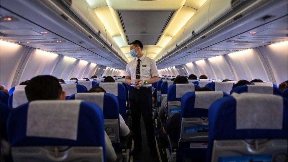 A flight attendant wearing a facemask as a preventive measure against the COVID-19 coronavirus checks passengers before a flight to the central Chinese city of Wuhan, at Pudong International Airport in Shanghai on July 14, 2020.