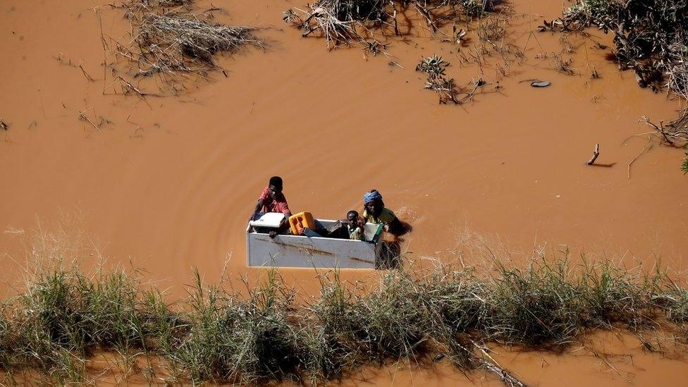 People holding on to some wooden furniture in Mozambique in flooded waters