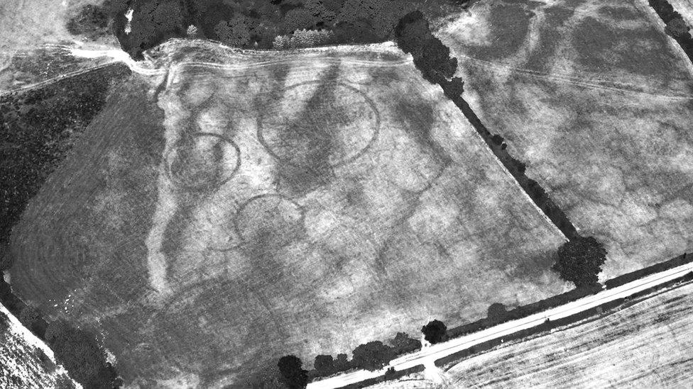 Black and white photograph shows four huge circles or barrows on the ground