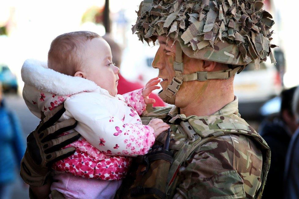 A soldier holds his baby as they look at each other