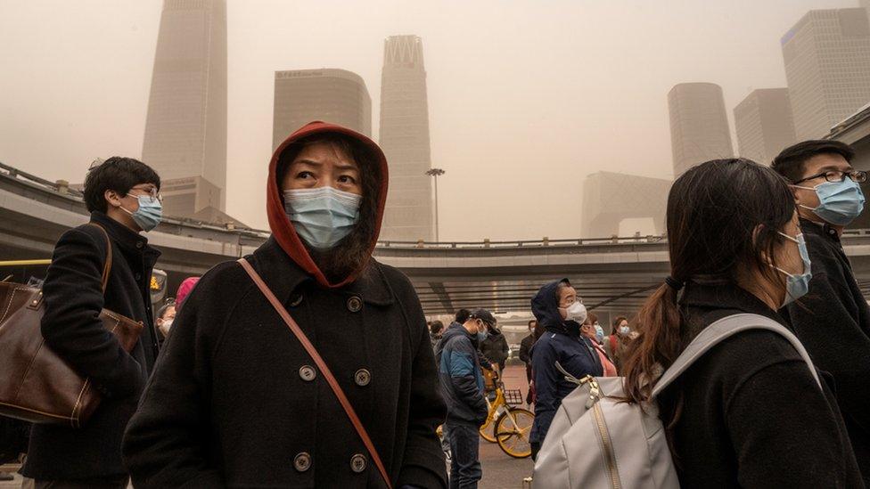 Commuters wear protective masks as they leave work in the Central Business District during a sandstorm on 15 March 2021 in Beijing