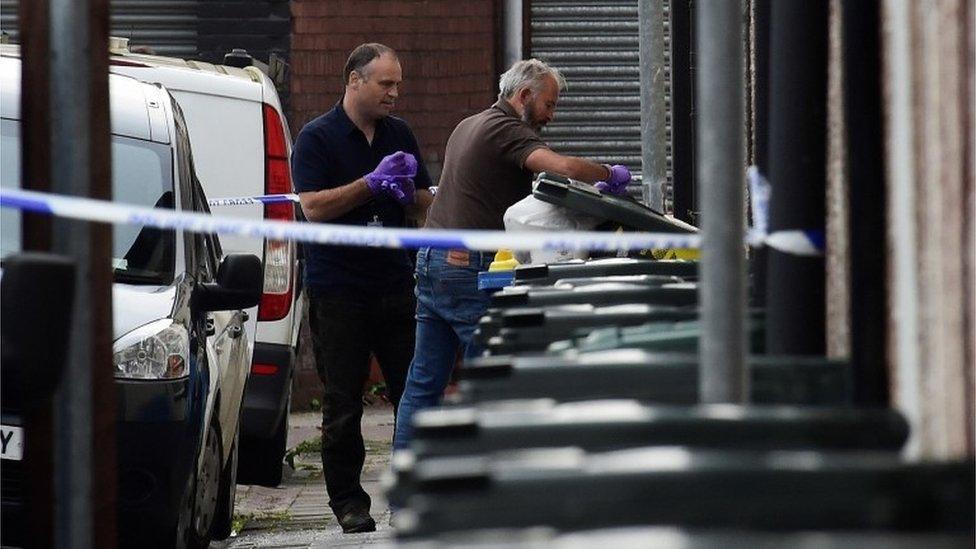 Investigators search rubbish bins behind a police cordon