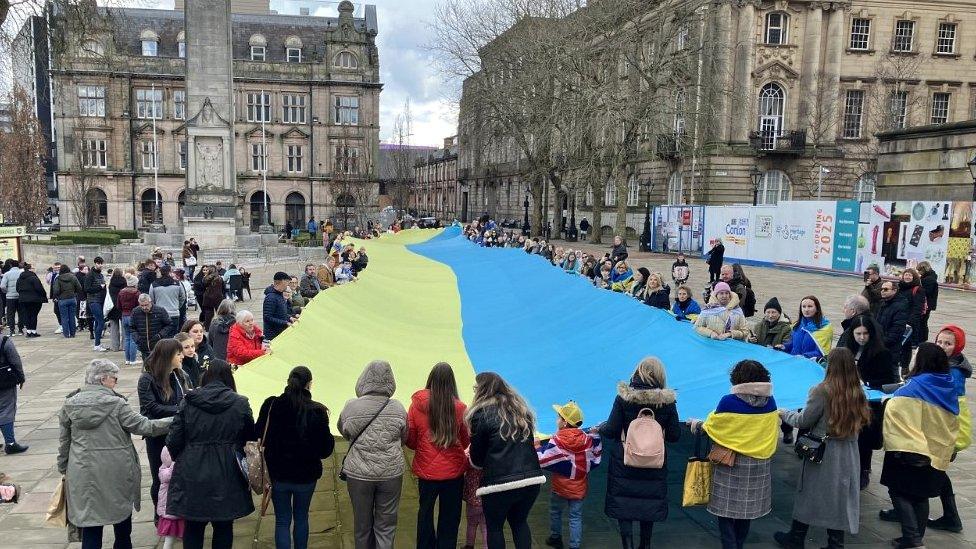 a crowd gathers around the large Ukrainian flag in Preston