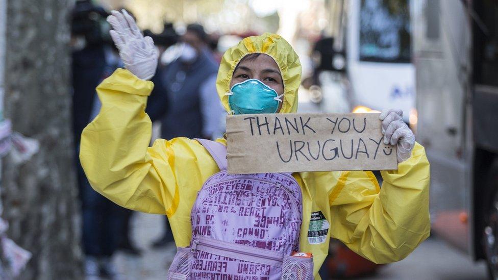 A crew member, having disembarked, holds a sign that says 'Thank you Uruguay'