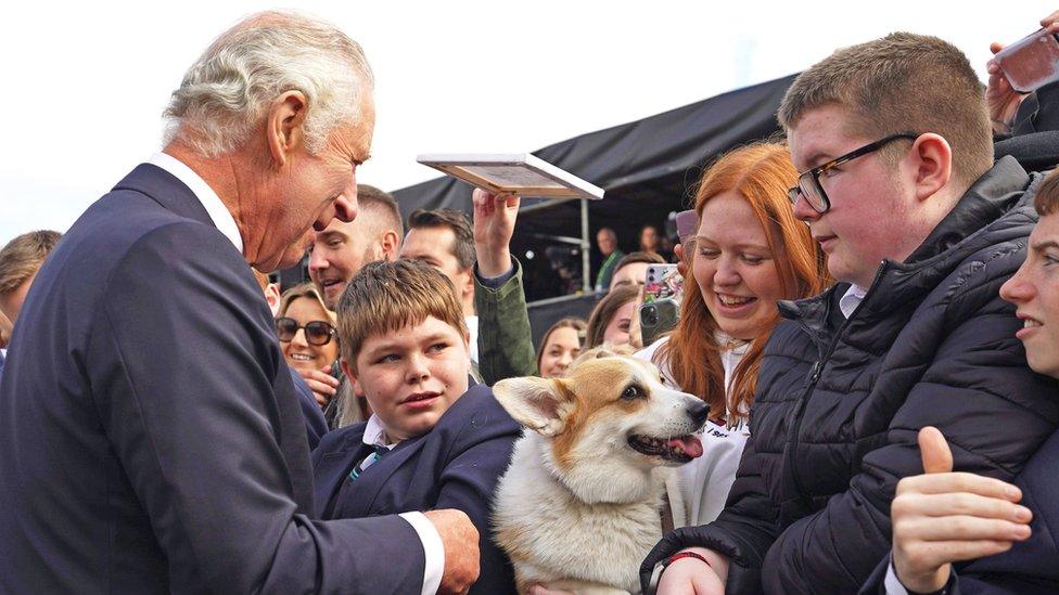 King Charles greets people and a corgi standing outside of Hillsborough Castle