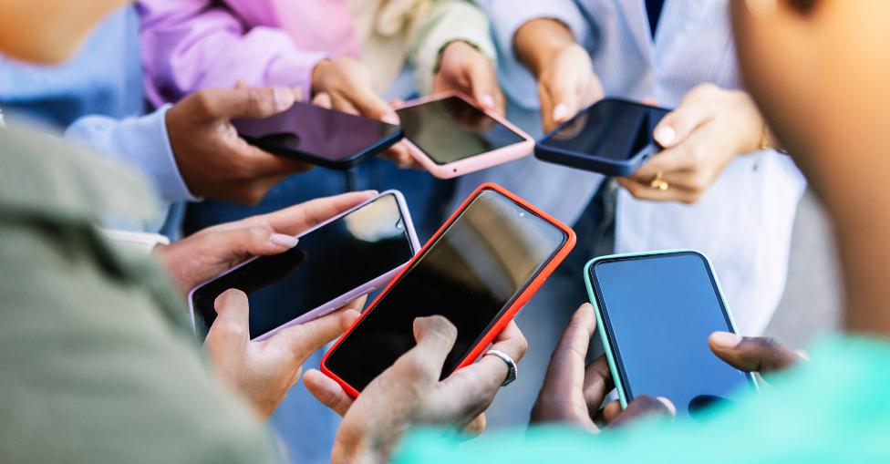 Young group of people standing in circle using mobile phones outside