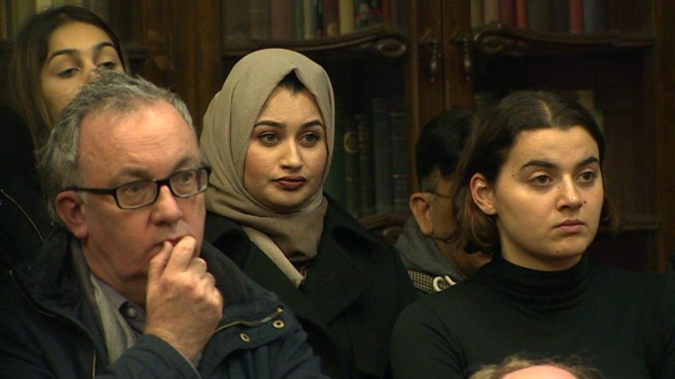 A woman wearing a head scarf listens to the speakers at the vigil