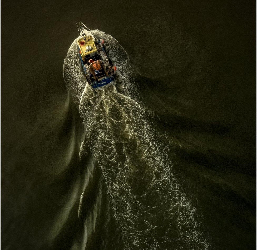 An aerial shot of a fishing boat leaving a trail of disturbance in the water