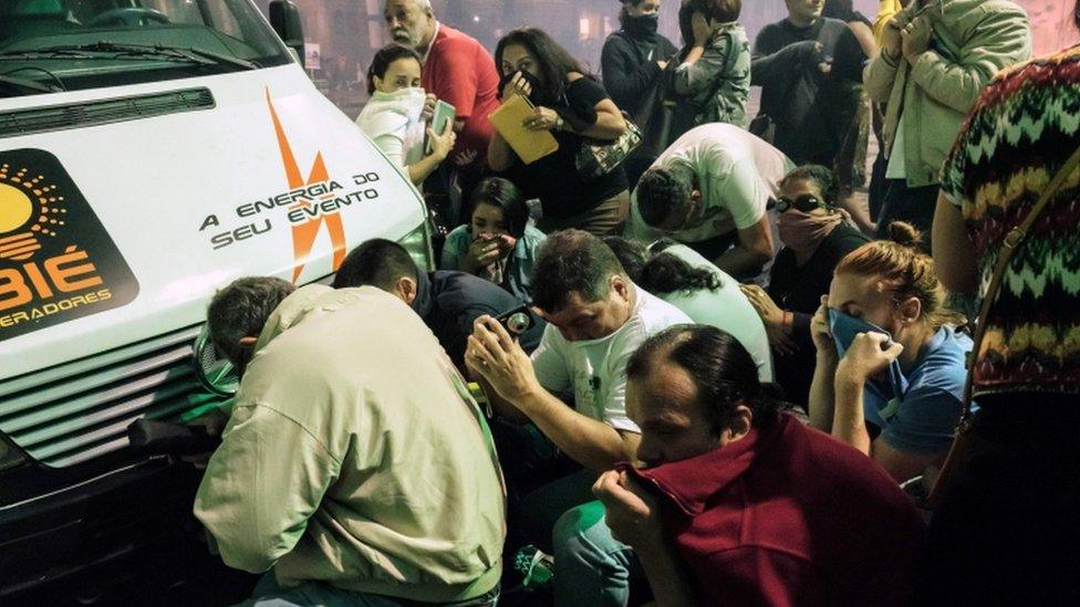 People hide behind a van in Rio to seek refuge from clashes between police and activists