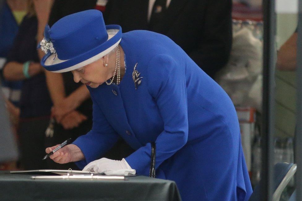 The Queen signs a book at the Grenfell fire relief centre