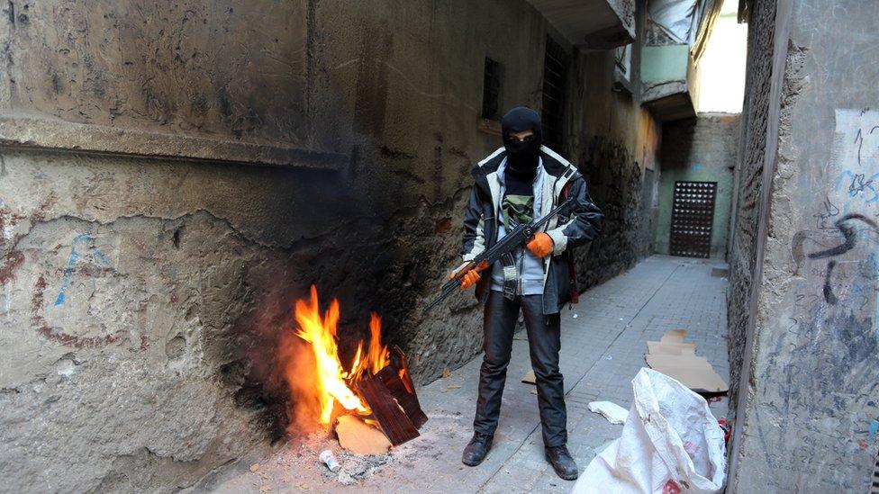 A PKK militant stands guard in an alley-way near a barricade as some thousands of people flee from the historic Sur district of the mainly-Kurdish city of Diyarbakir, Turkey, Wednesday, Jan. 27, 2016