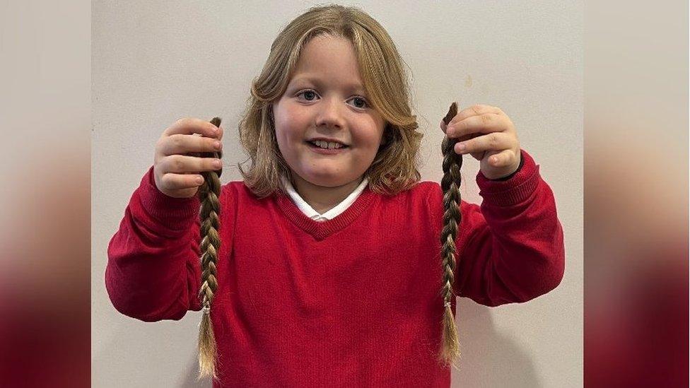 Noah smiling whilst holding two plaits of his hair up