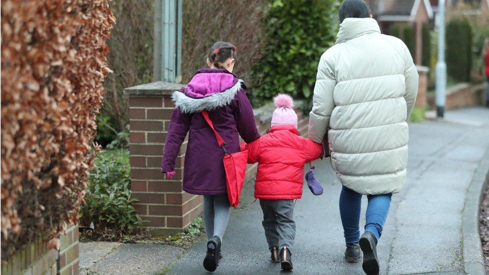 Two children and an adult walk to school