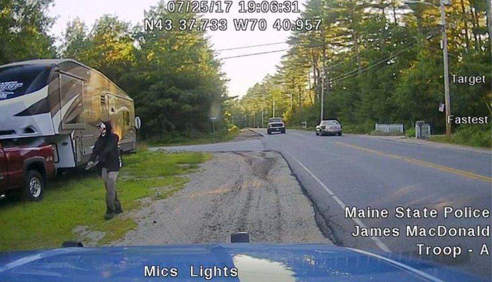 A picture released by Maine State Police shows a man strolling down a street in Hollis, Maine, wearing a clown mask and with a machete taped to his amputated arm