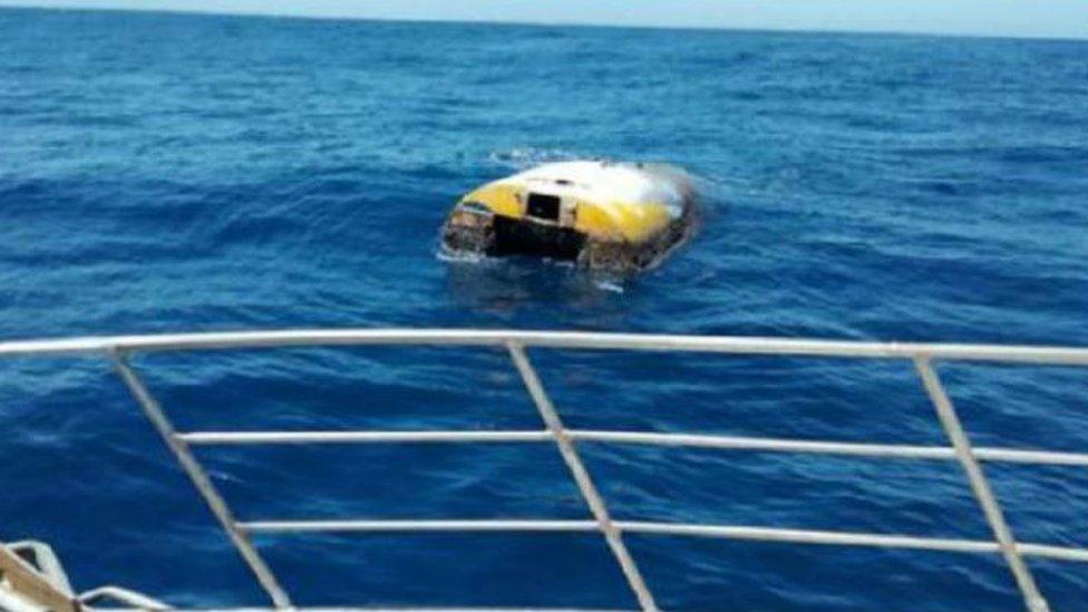 The upturned vessel Wild Eyes, seen from behind the rail of another boat