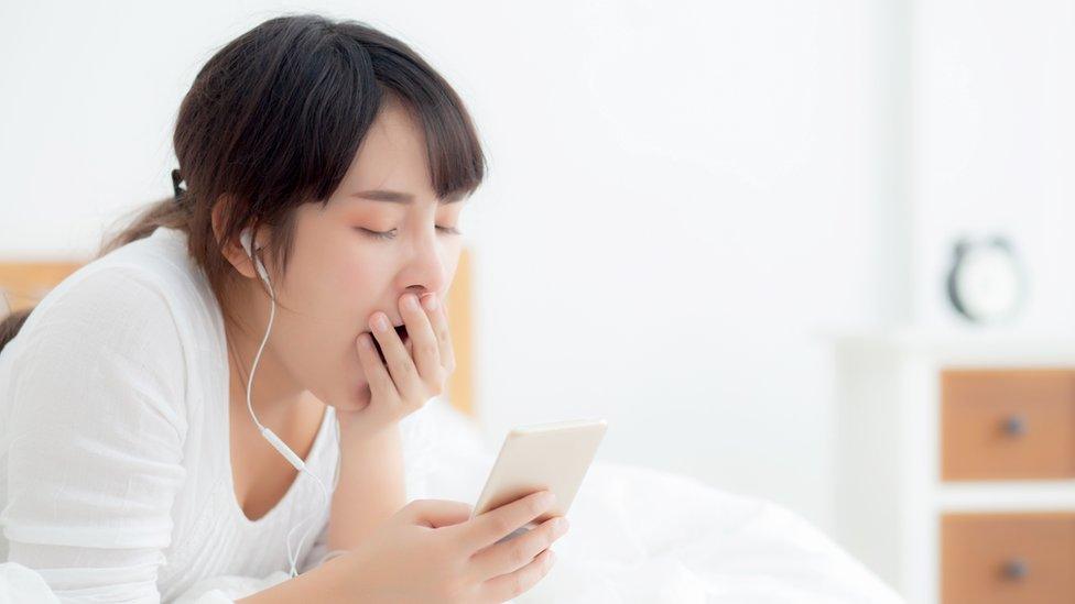 Yawning teenage girl looking at her phone