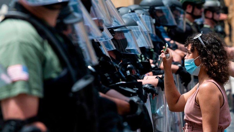 A protester hold up her phone to show a line of police in riot gear something on the screen