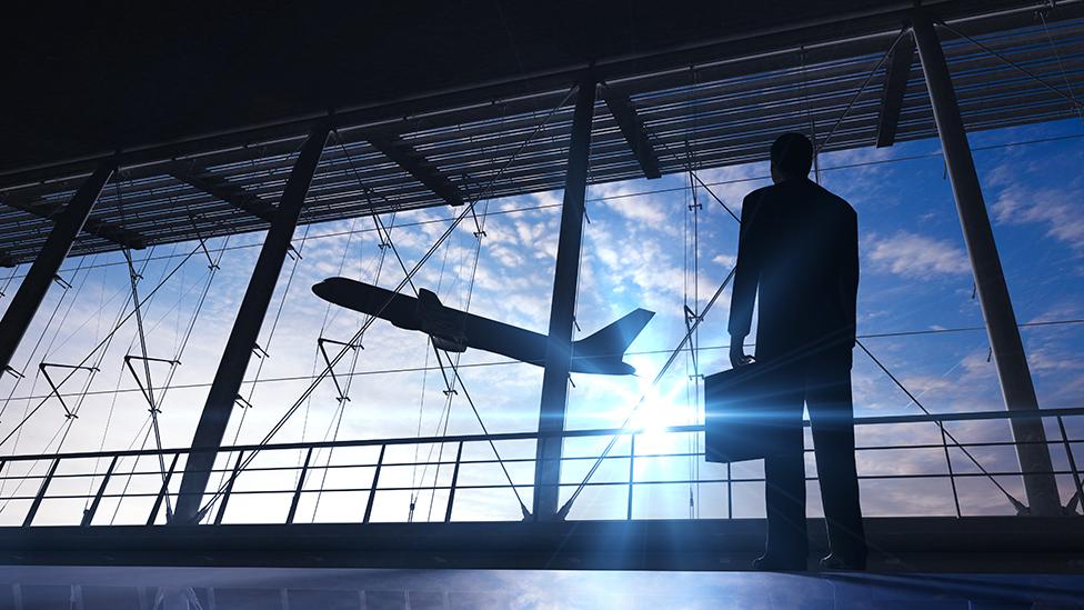 Traveller in airport terminal with briefcase watching plane take off