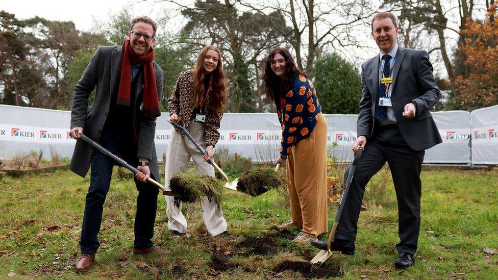 four people standing with shovels