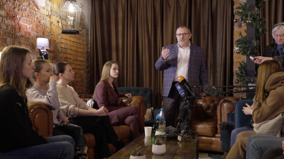 Women sit on sofas listening to presidential hopeful Boris Nadezhdin stand up and speak