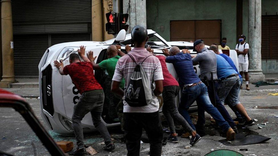 People push an overturned car in the street in the framework of a demonstration against Cuban President Miguel Diaz-Canel in Havana, on July 11, 2021.