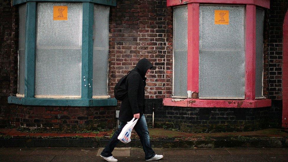 Man walking past some boarded up houses