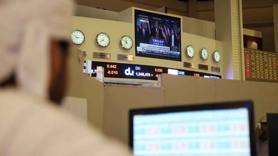 A screen showing Donald Trump is seen on a TV as a trader monitors stock information at Dubai Financial Market, in Dubai (9 November 2016)