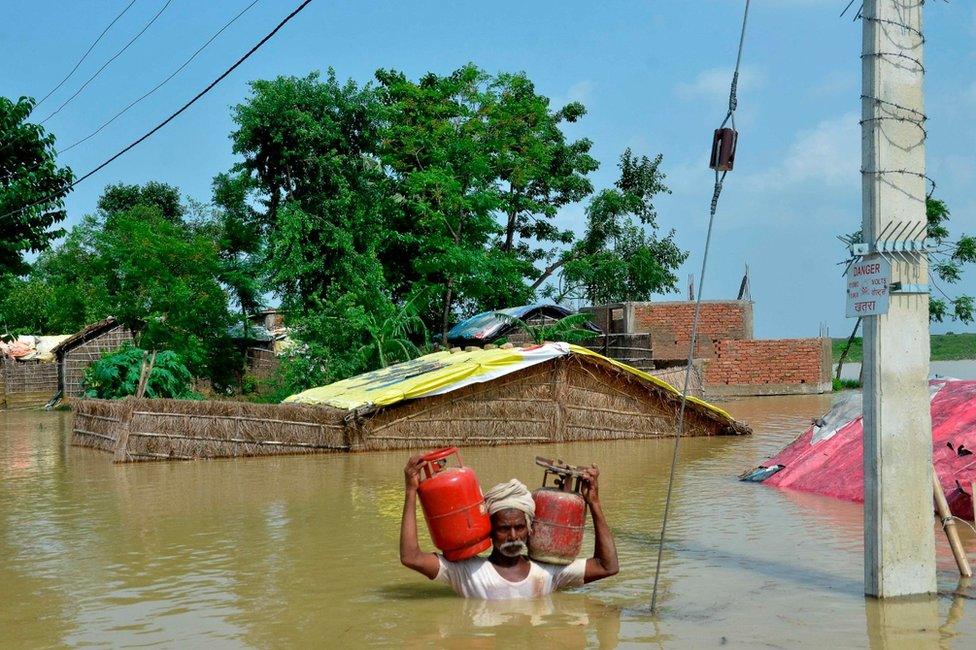 An Indian resident carries gas canisters as he wades through a flooded area following heavy monsoon rains in Muzaffarpur in the Indian state of Bihar.