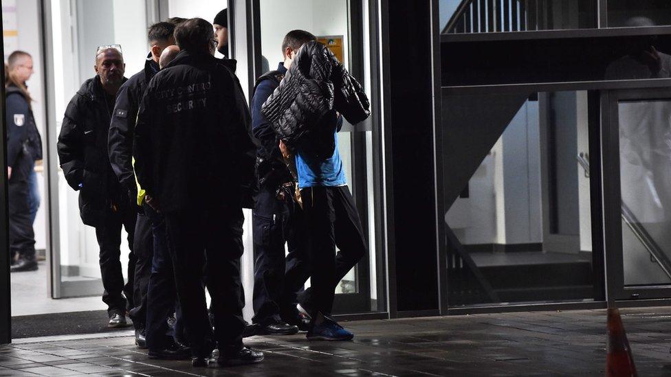 A man is led away by police with a coat hanging over his face