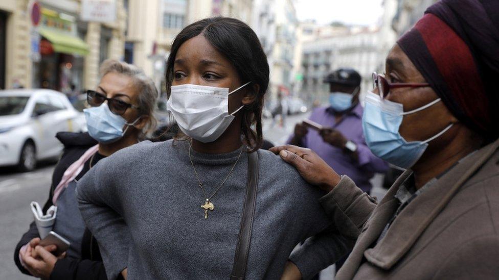 Locals wearing face masks look on near the scene of the attack