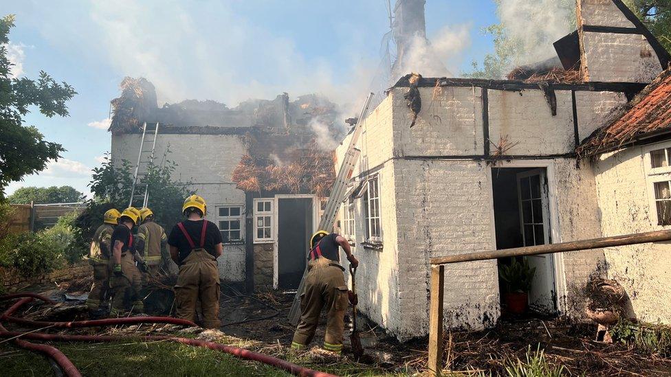 House with most of the roof burnt away. Firefighters works on the ground